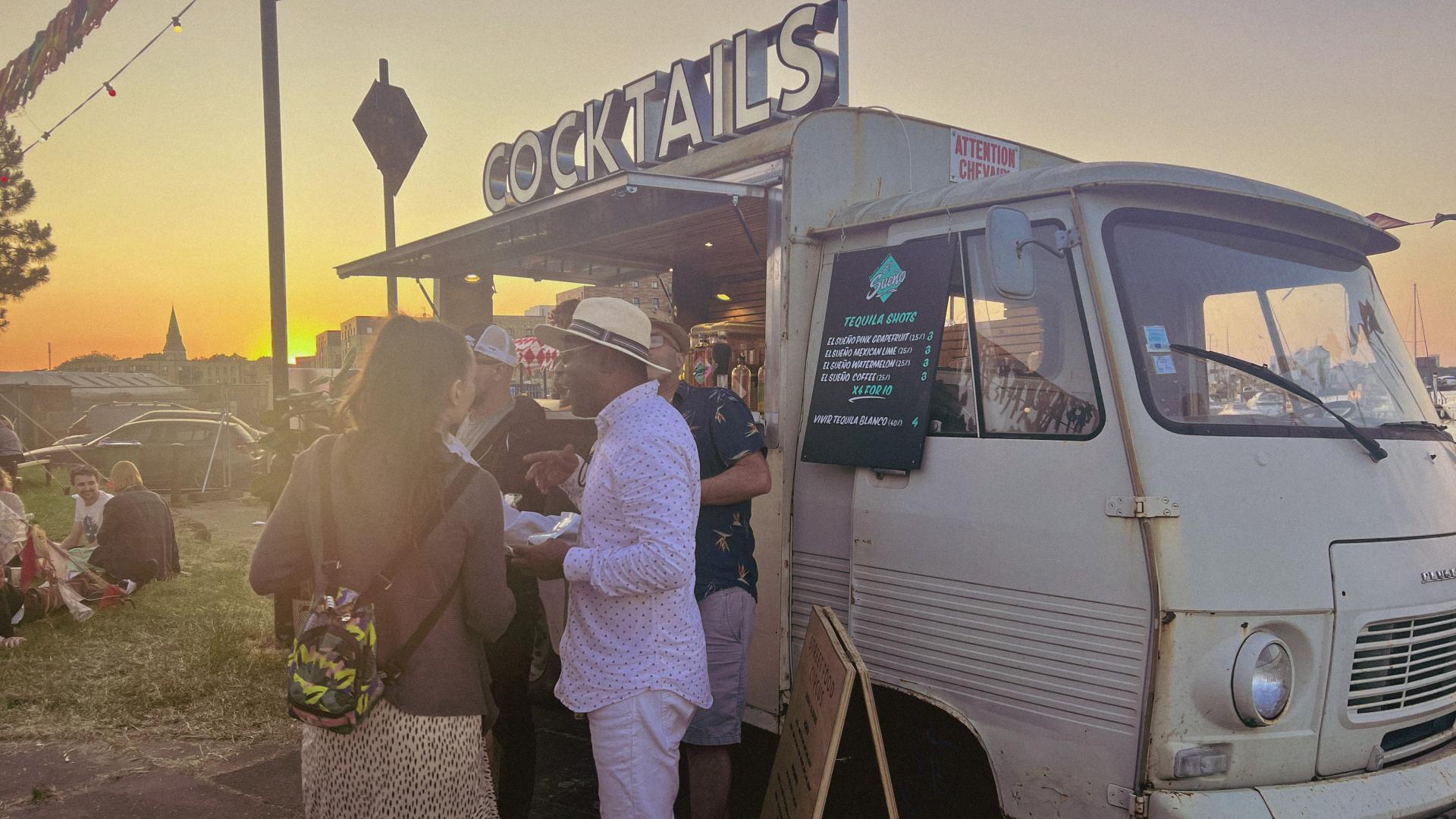 a group of people chatting stood infront of a cocktails vendor van